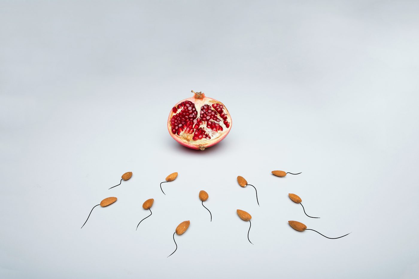 A halved pomegranate above almonds arranged with drawn tails